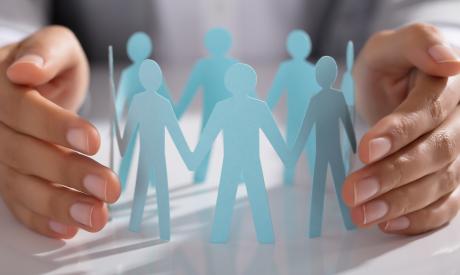 Ένα άτομο σχηματίζει έναν κύκλο με κομμένες φιγούρες από χαρτί, που συμβολίζουν την ενότητα ή την προστασία της ομάδας.